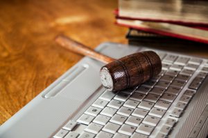 Wooden Judge's gavel lying on top of a laptop computer table inside a courthouse. Legal system, technology, white collar crimes, online auction concepts. No people.